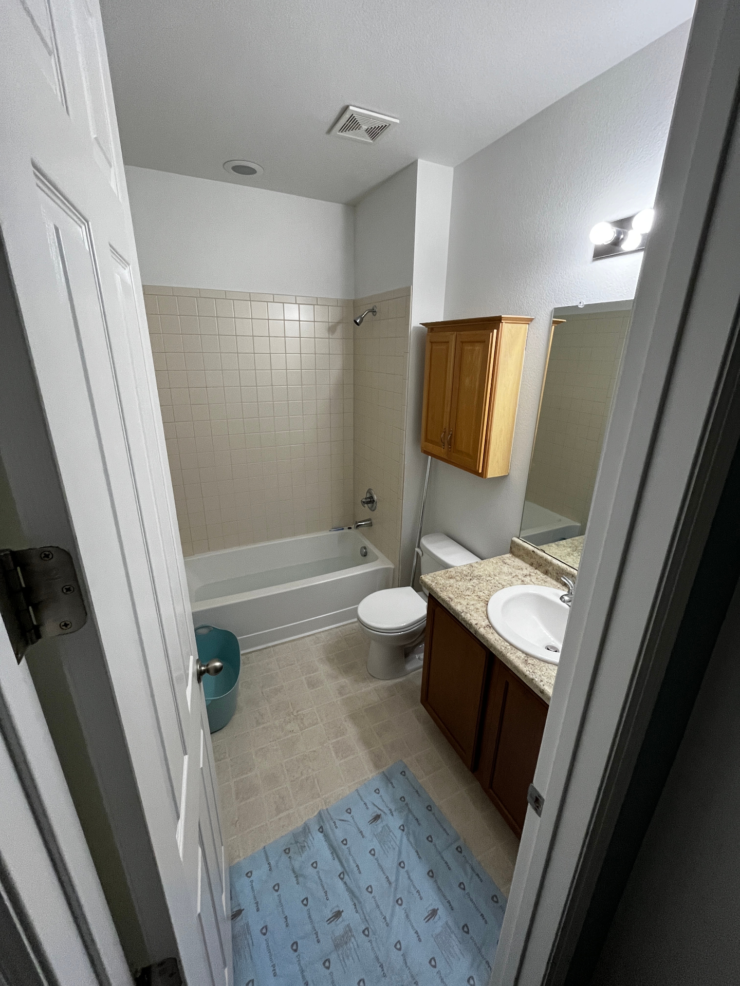 Bathroom before remodel with beige tile surround and wood vanity