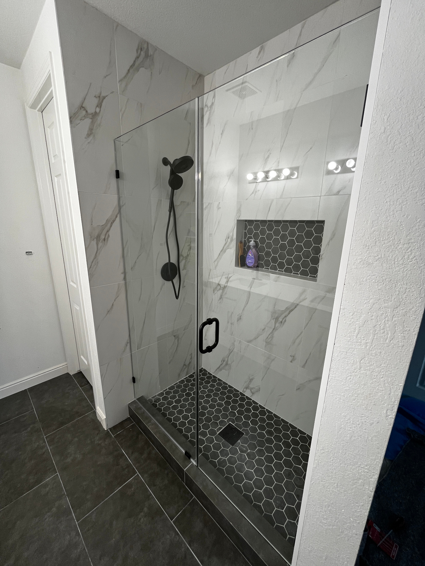 Frameless glass shower with marble walls and hexagon mosaic floor