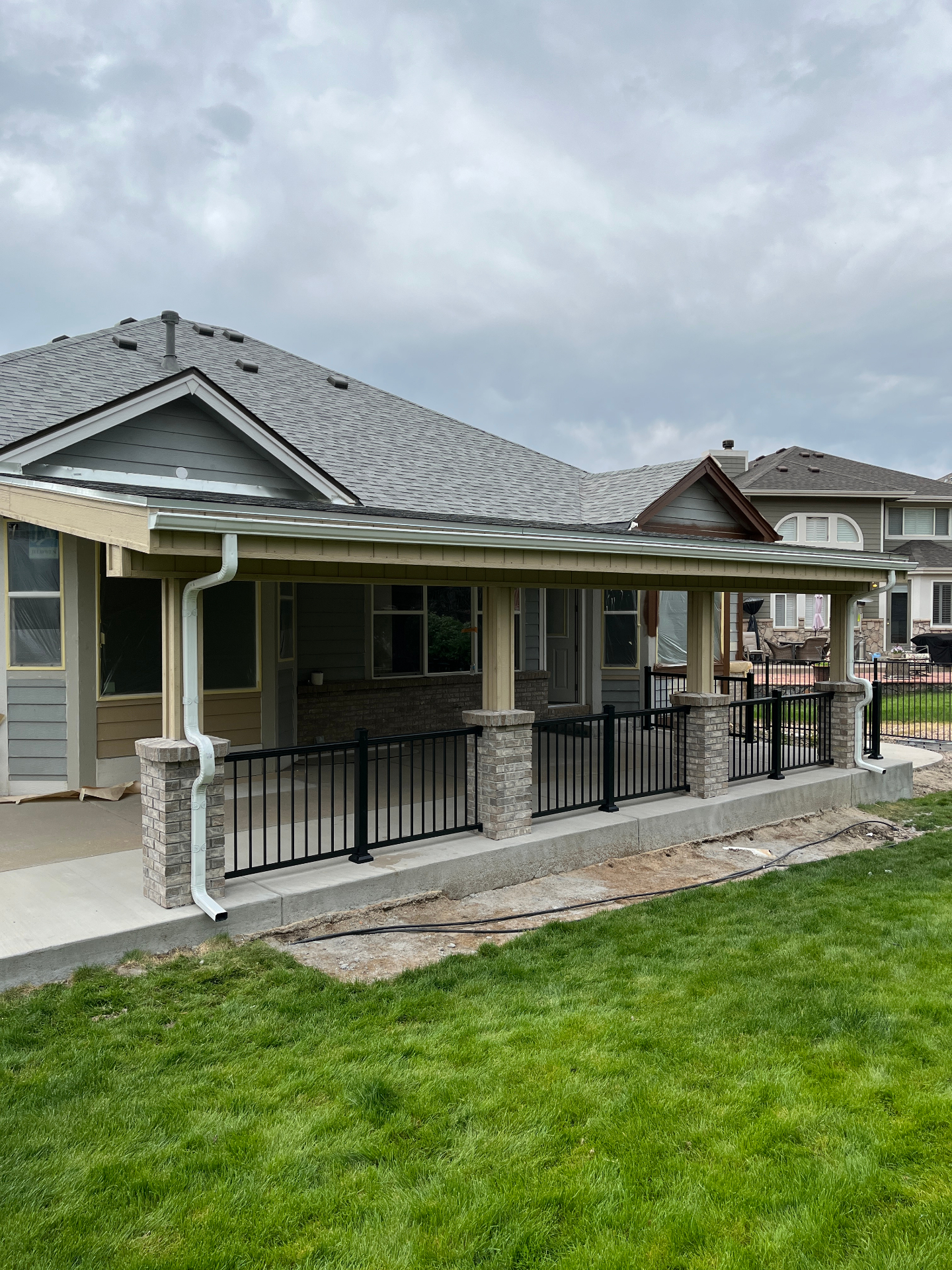 Large finished covered patio with black railing, masonry columns, and gray roofline