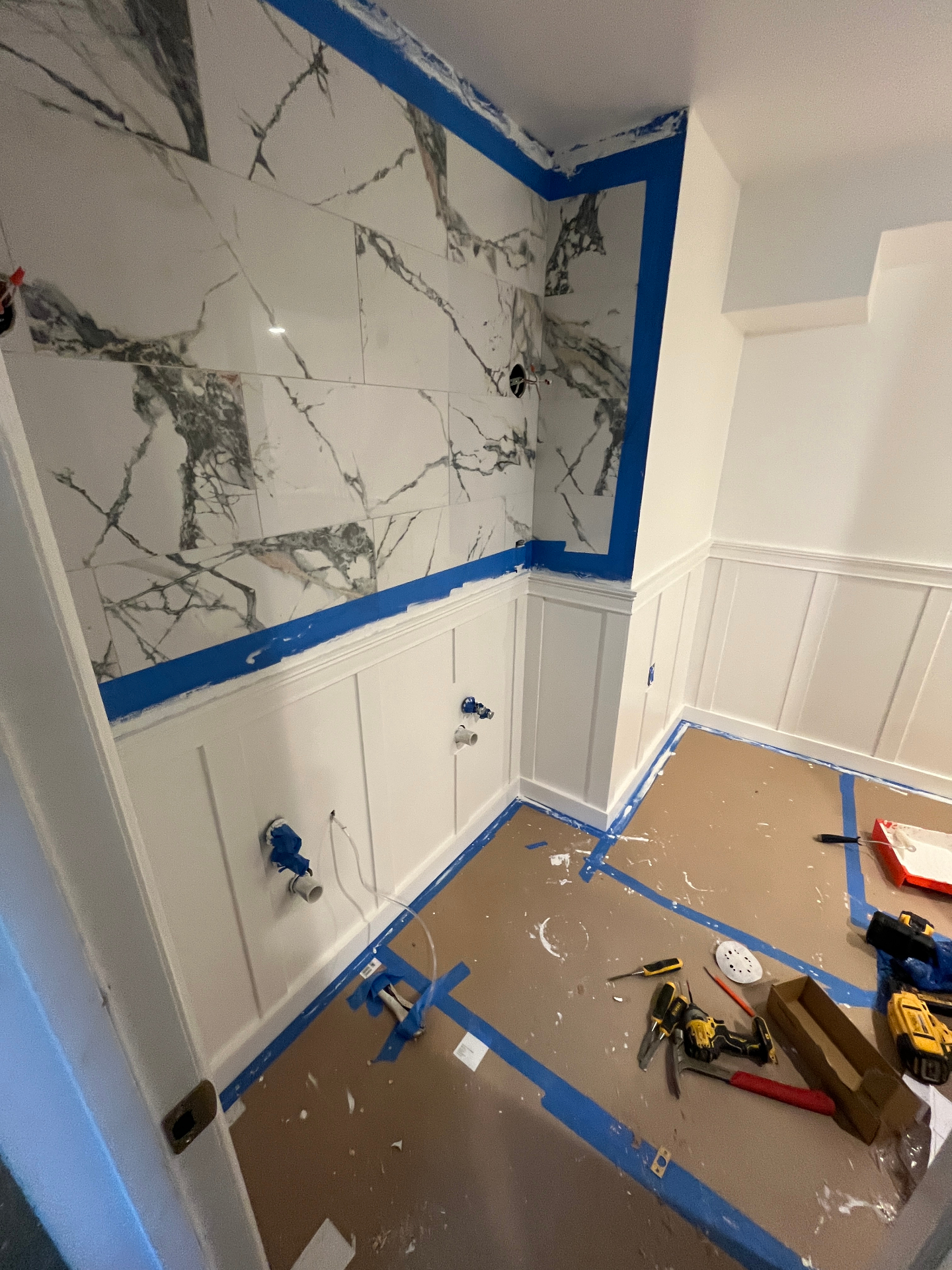 Marble bathroom with tile set and taped off, board-and-batten wainscot painted white before fixtures
