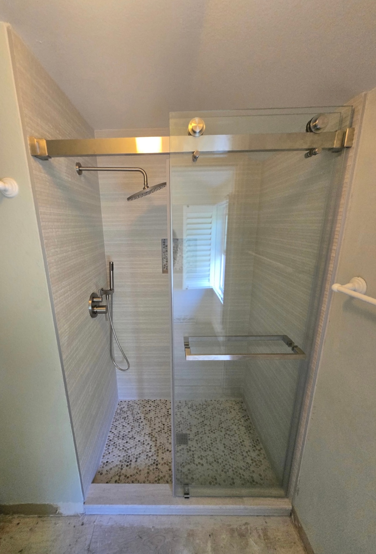 Walk-in shower with frameless sliding glass door, linear tile walls, and pebble mosaic floor