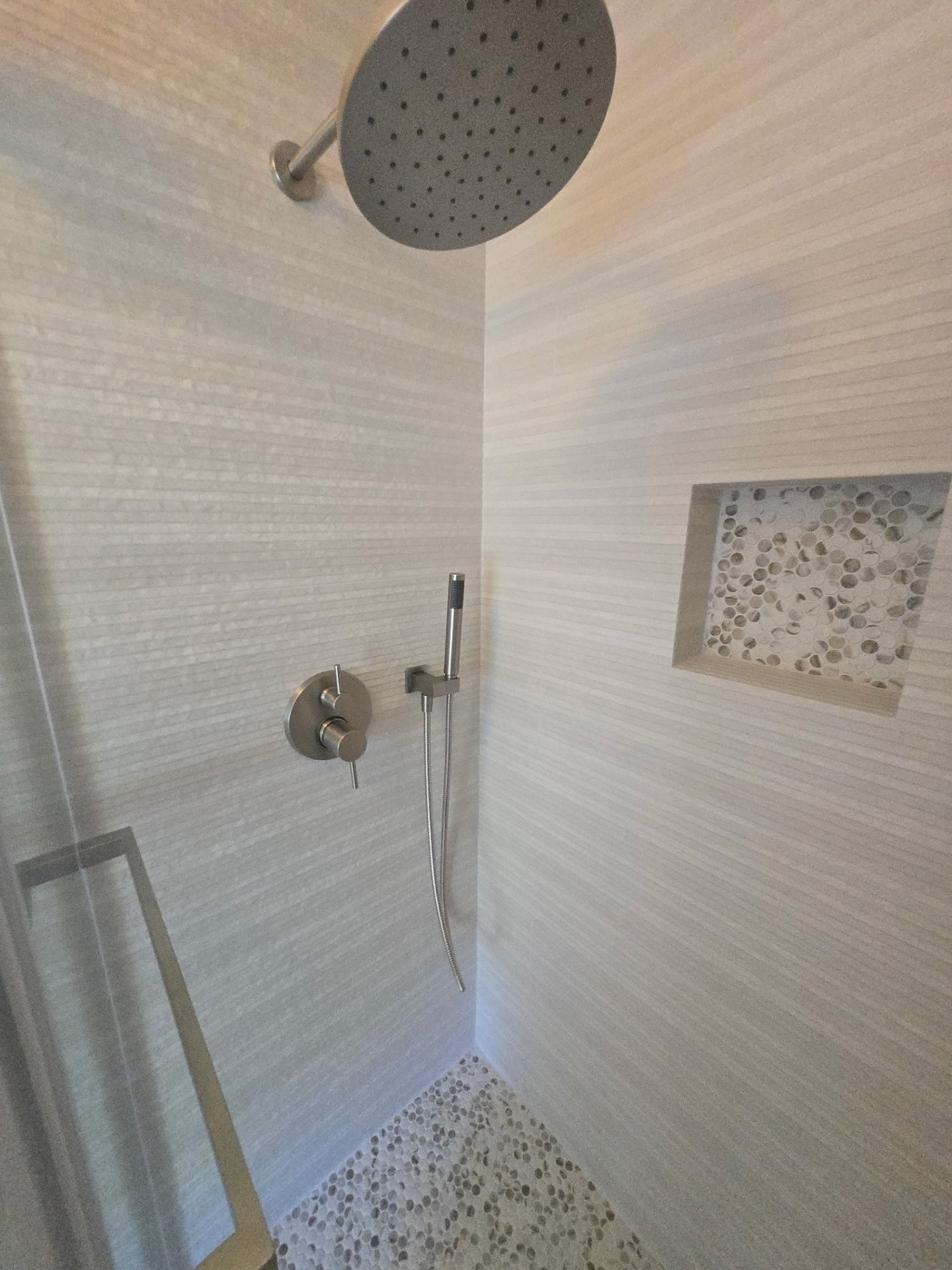 Walk-in shower interior with brushed nickel rainhead, handheld wand, and pebble-tile niche