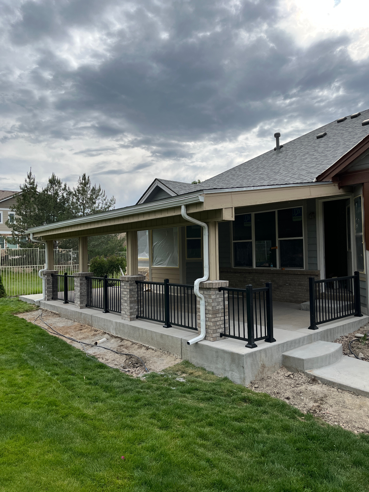 Covered patio addition viewed from the backyard with black metal railing and stormy sky