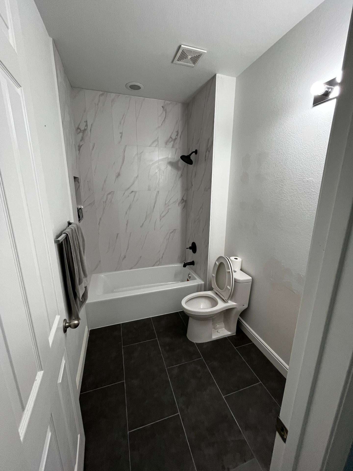 Bathroom after remodel with marble-look shower walls and dark floor tile