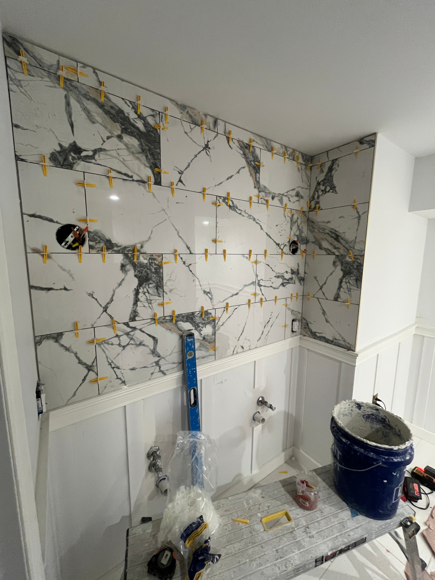 Arabescato marble large-format tile being installed with leveling clips above board-and-batten wainscot