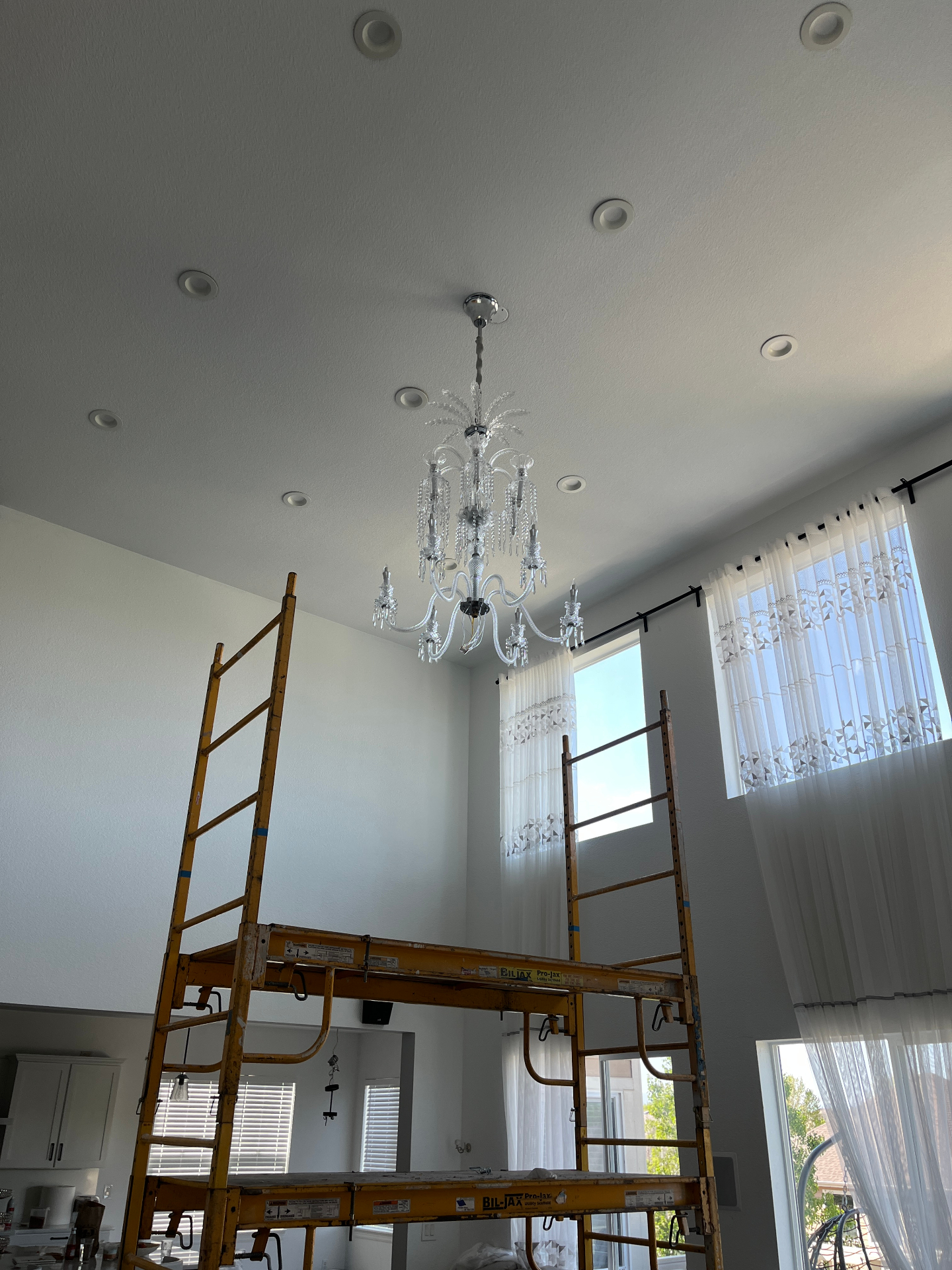 Crystal chandelier being installed in a tall great room with scaffolding in place