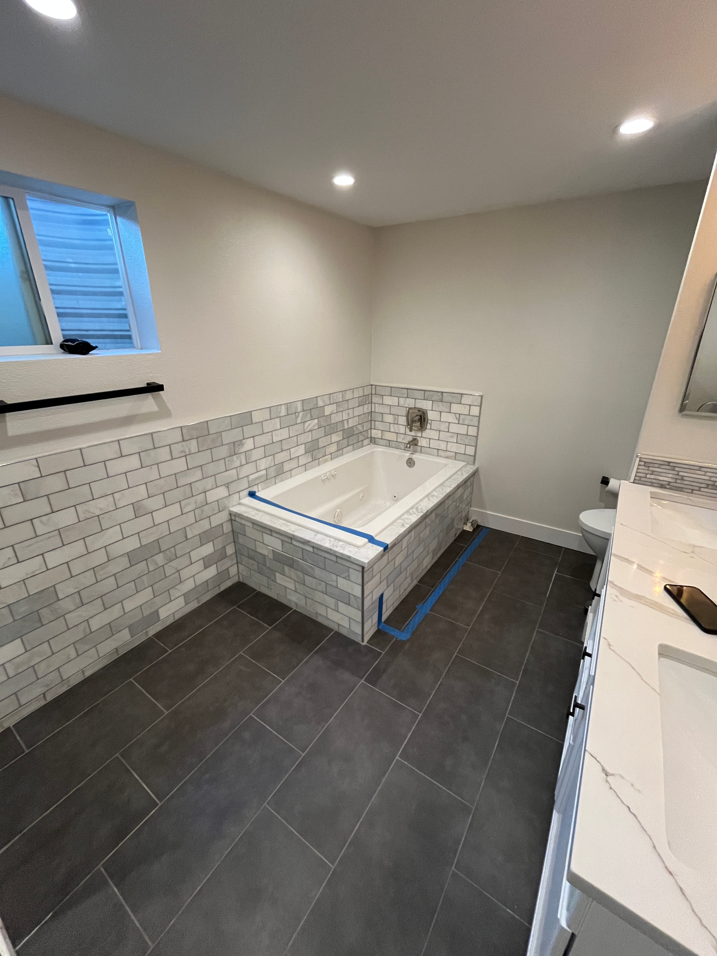 Bathroom remodel with a marble-tile jetted soaking tub, dark floor tile, and quartz vanity