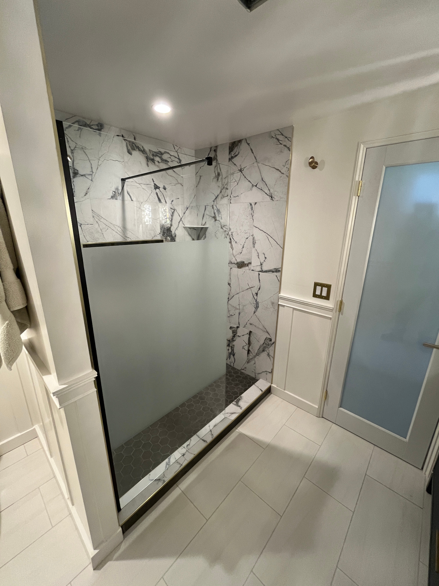 Finished walk-in marble shower with frosted glass panel, brass trim, and hexagon mosaic floor
