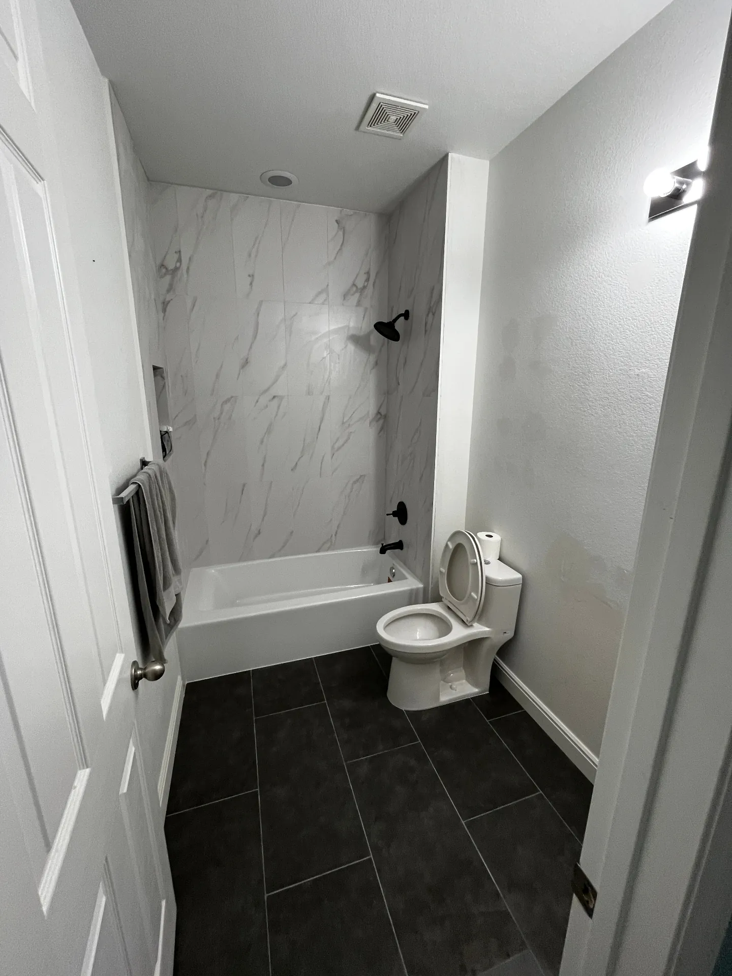 Bathroom after remodel with marble-look shower walls and dark floor tile