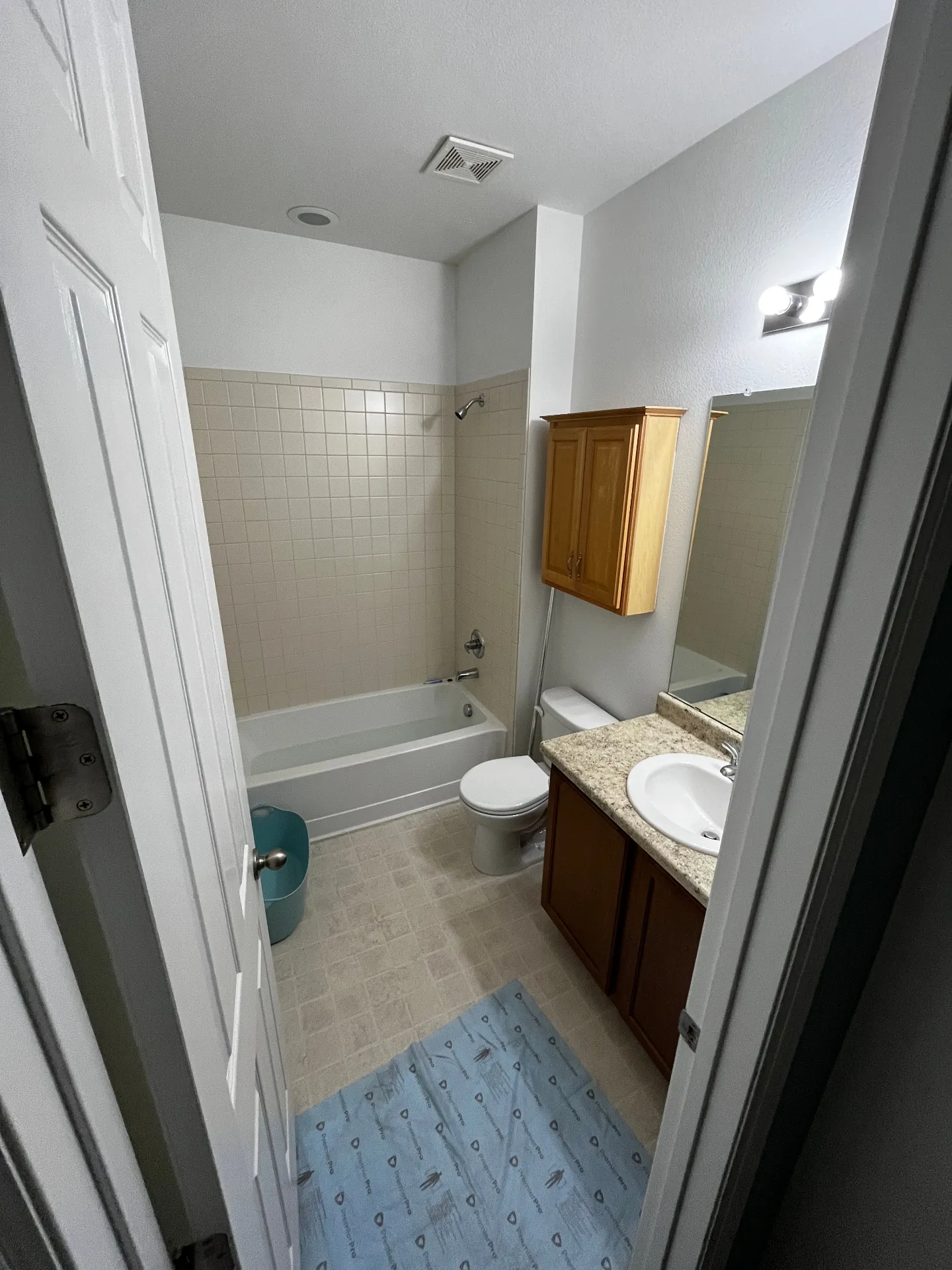 Bathroom before remodel with beige tile surround and wood vanity