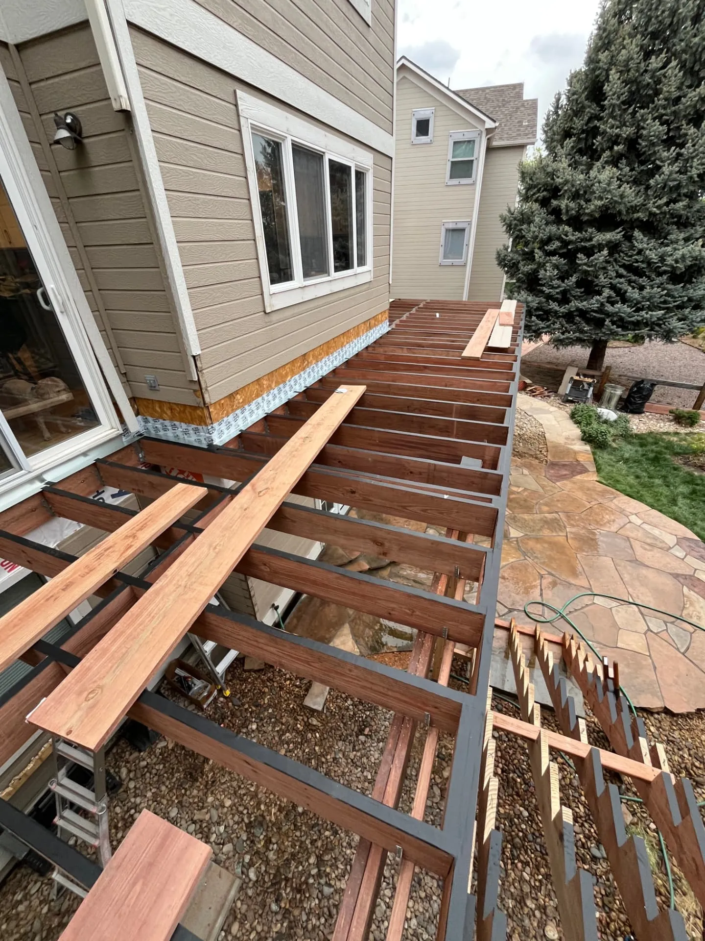 Elevated redwood deck framing with taped joists and a ledger tied into the home above a flagstone patio