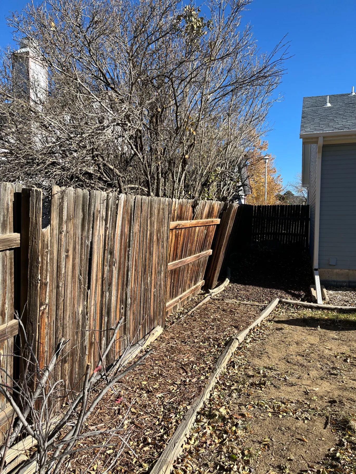 Old weathered wood fence leaning and falling apart along a side yard before replacement