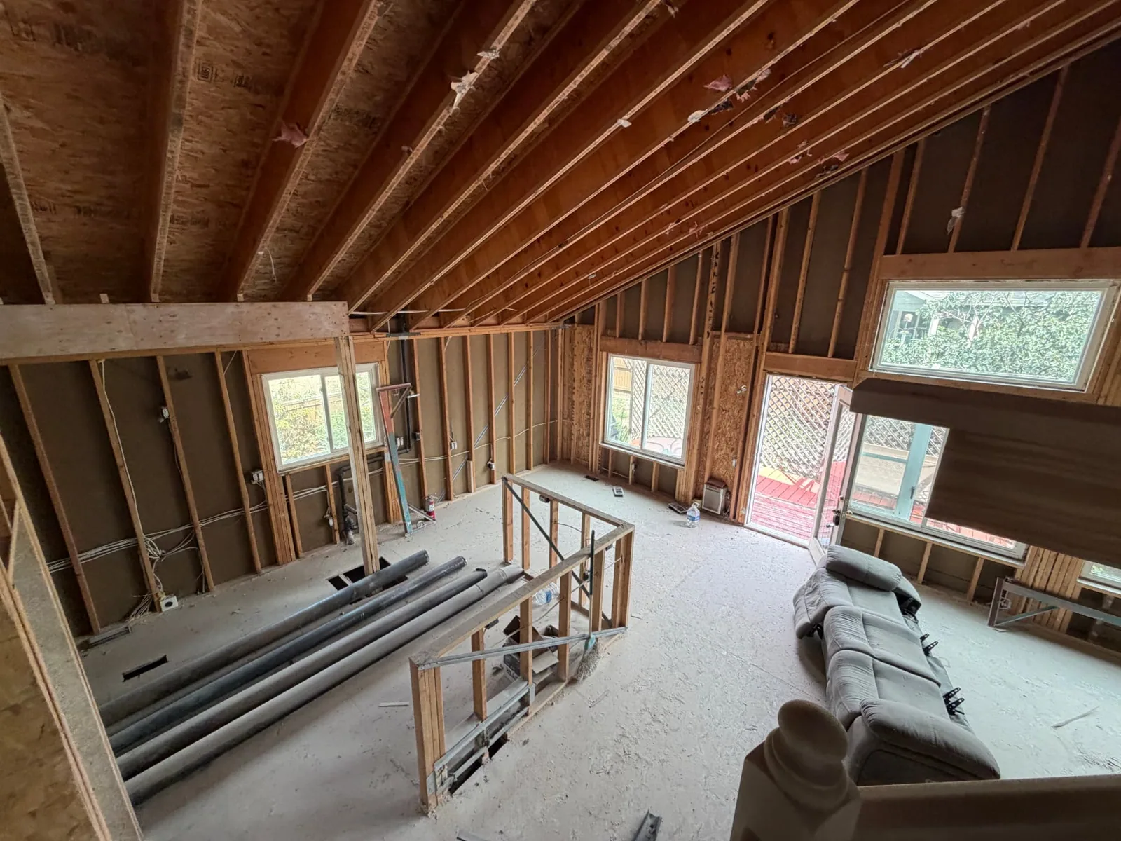 Great room framing with vaulted rafters, new window openings, and stacked plumbing stock during a fire rebuild
