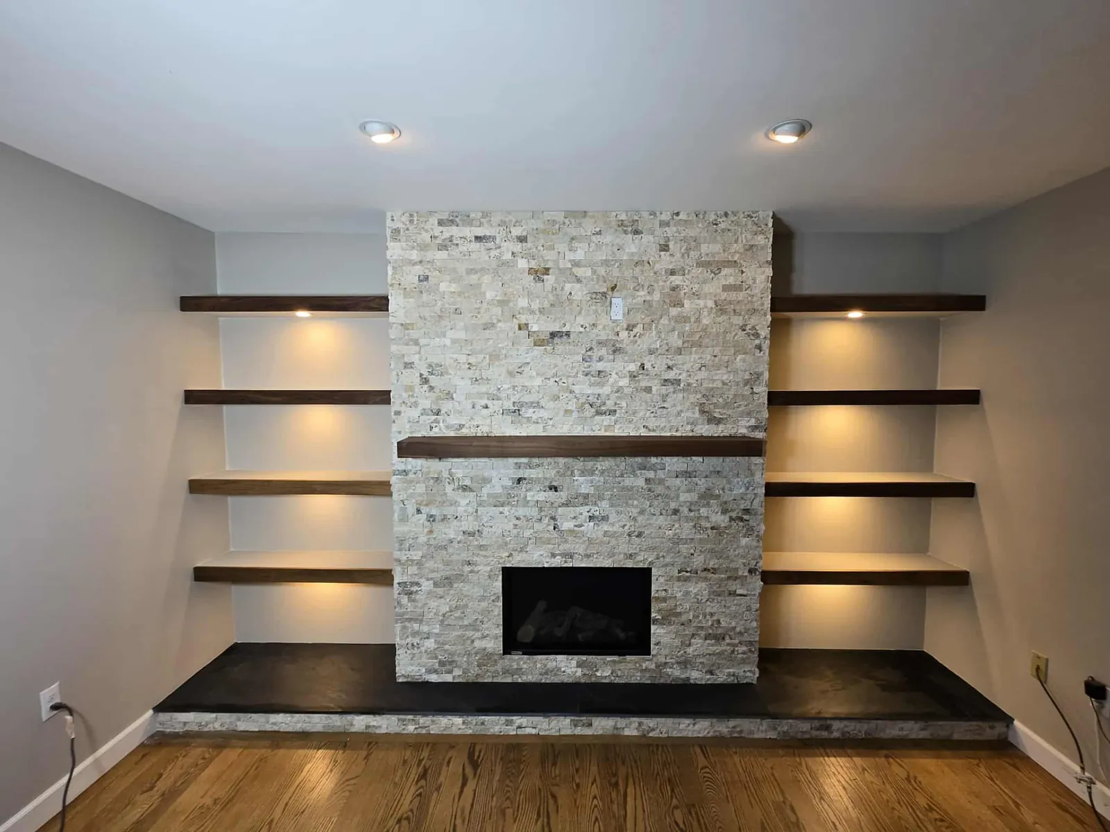 Finished stacked-stone fireplace with floating walnut shelves, under-shelf lighting, and slate hearth