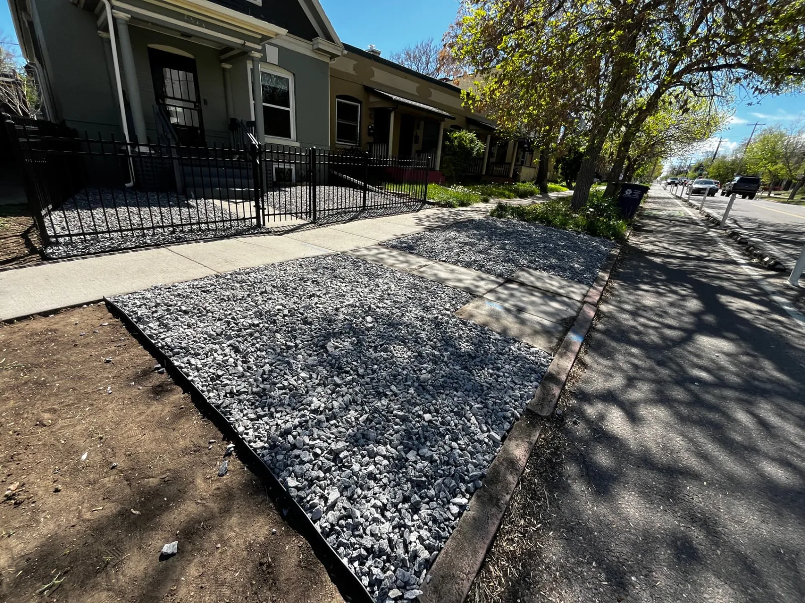 Crushed gravel strips with steel edging installed along a Denver sidewalk on a freshly graded parkway