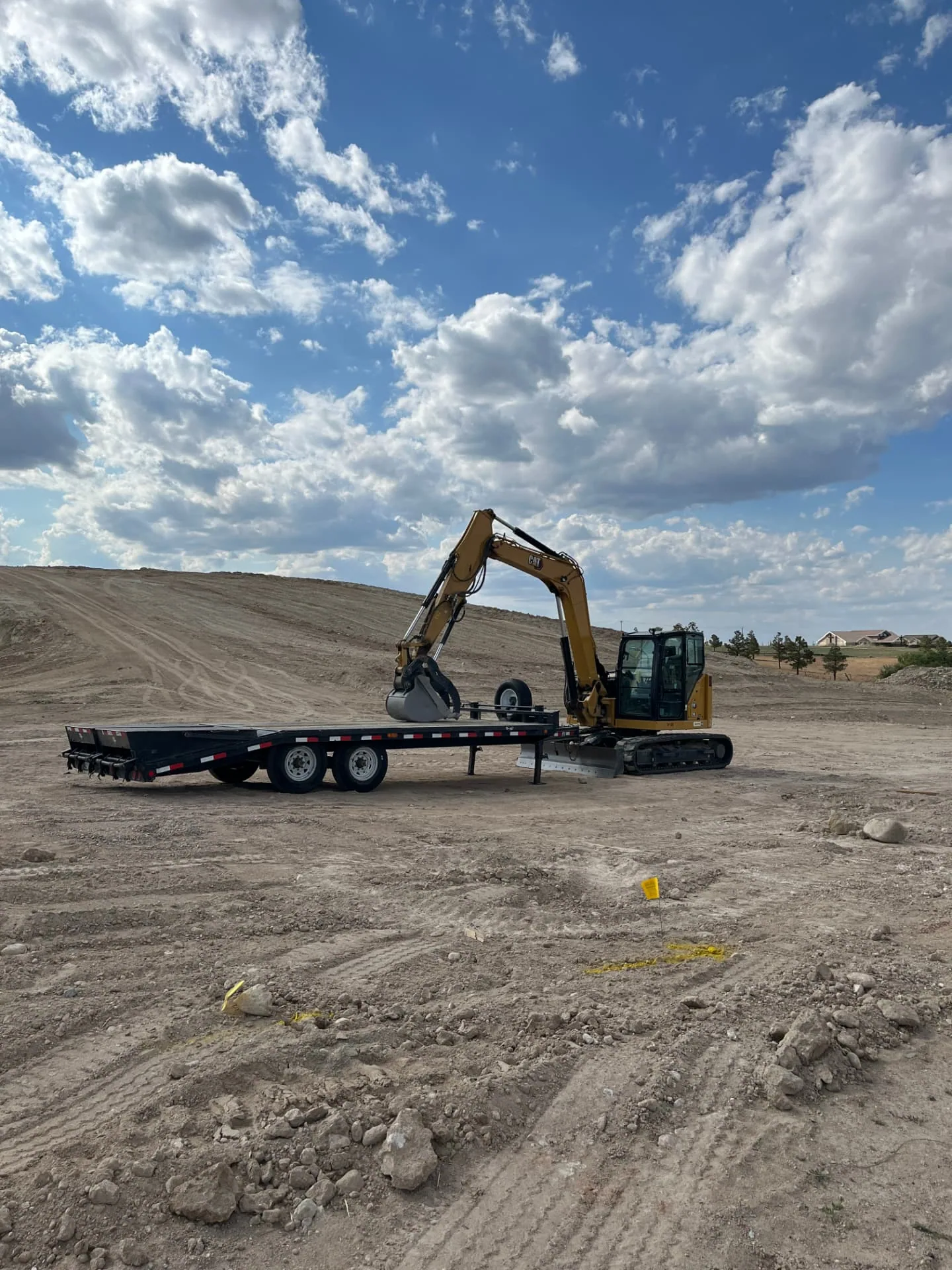 Compact excavator staged beside a lowboy trailer on a graded dirt work site
