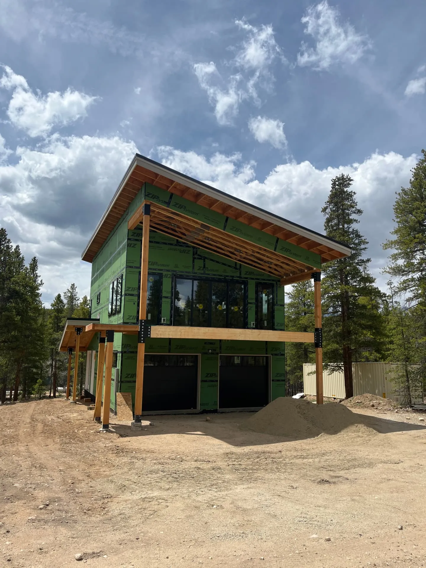 Mountain-modern custom home under construction with ZIP System sheathing, timber posts, and a shed roof in the pines