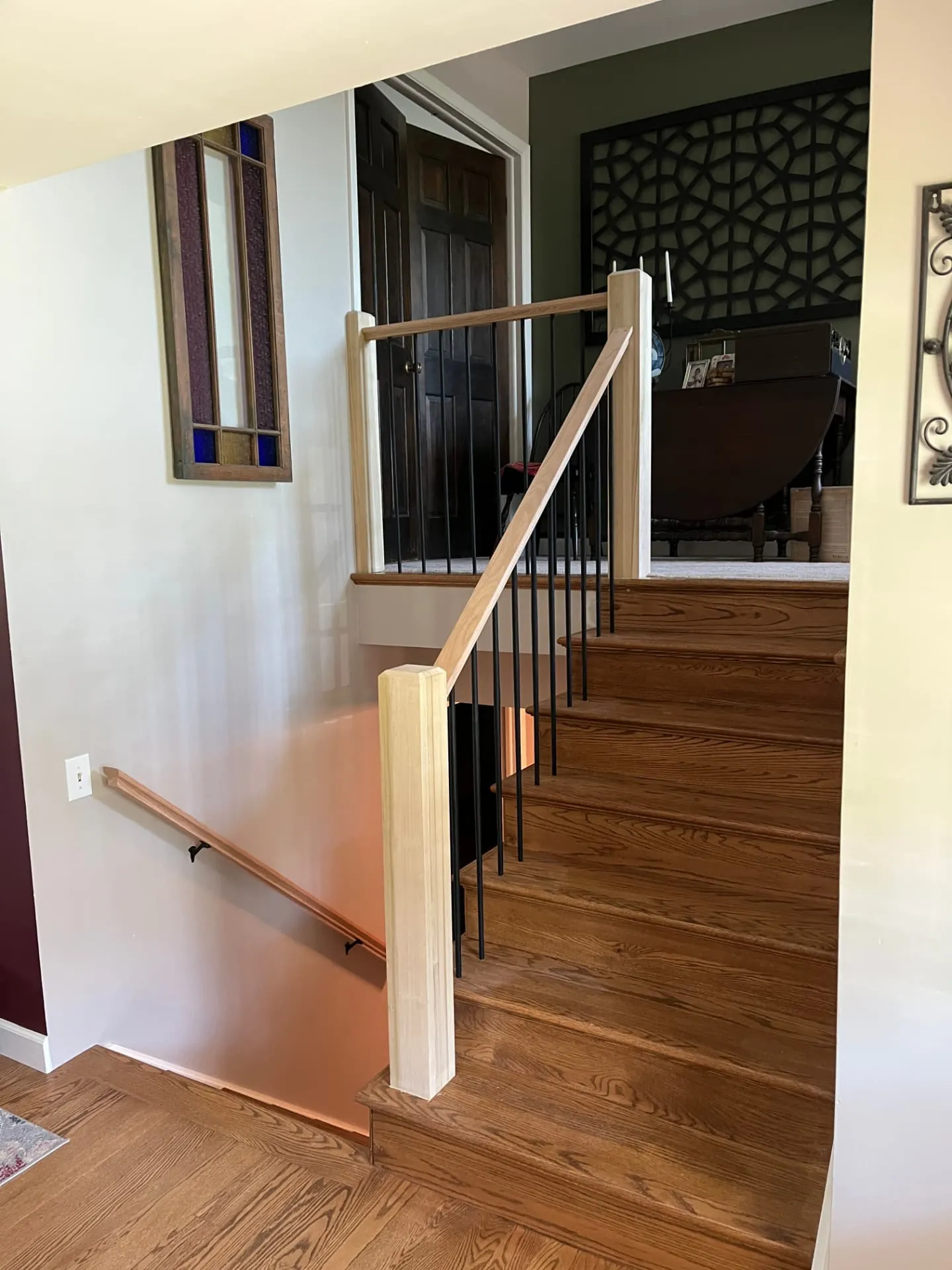 Finished oak stair rail with square newel posts and black iron balusters in an open entry