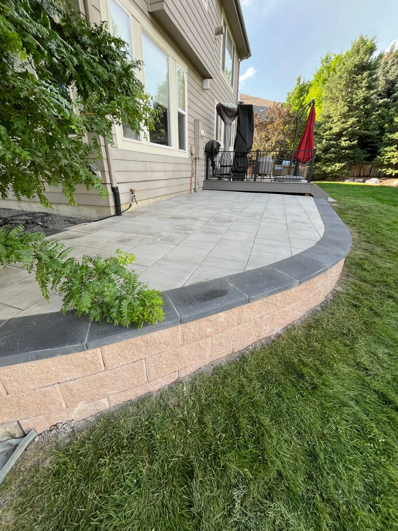 Finished raised paver patio with charcoal coping and planted locust by the deck
