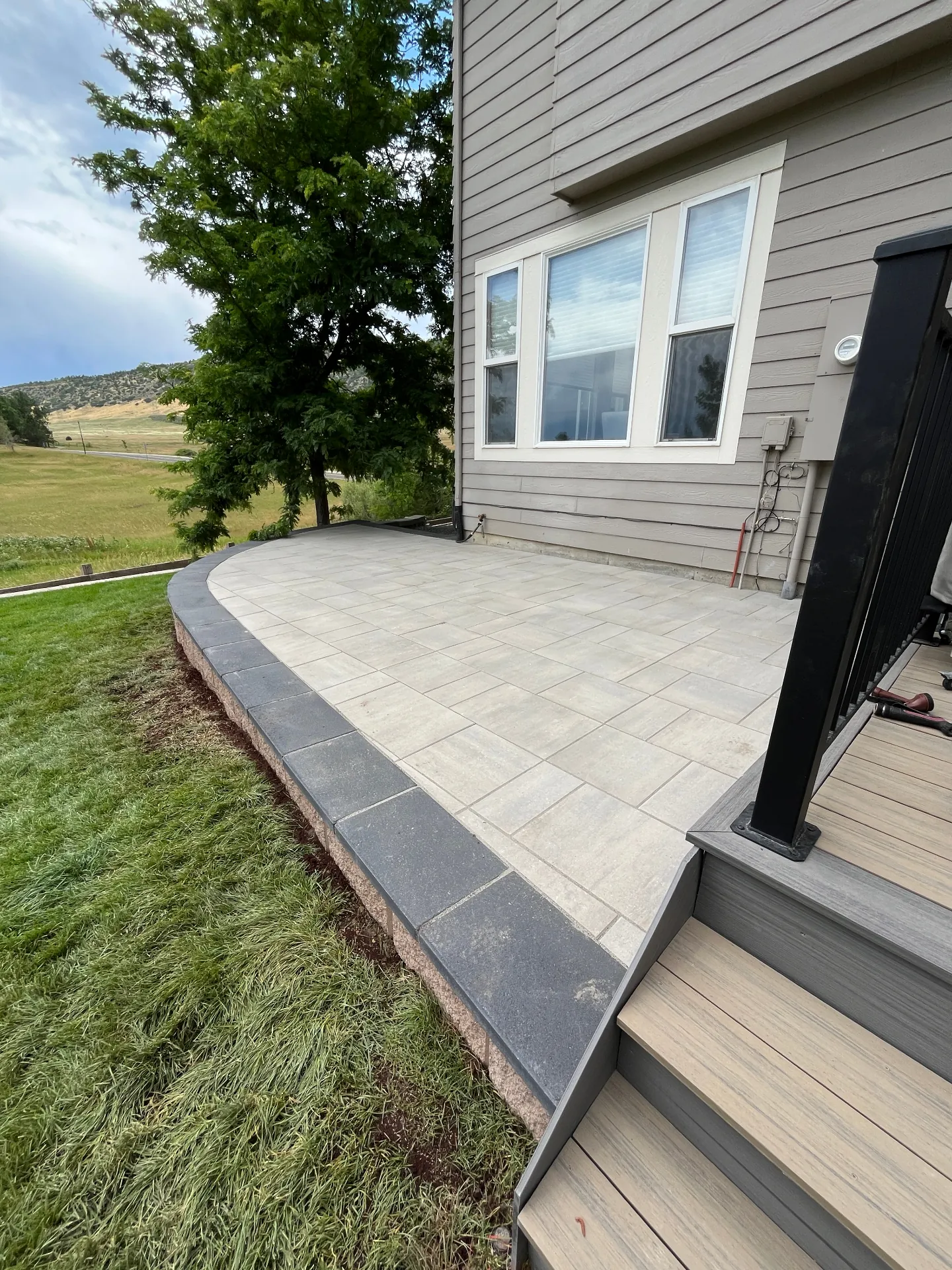Finished curved paver patio next to composite deck steps with mountain views beyond