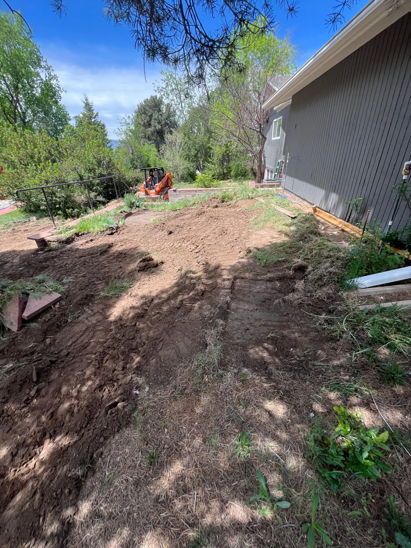 Compact track loader regrading a sloped side yard alongside a Front Range home